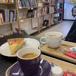 Koffiekopjes en een stuk cake op tafel in de lunchroom, met boekenkasten op de achtergrond