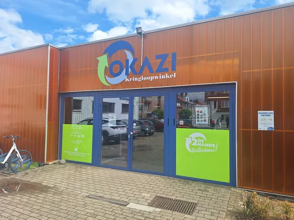Voorgevel van kringloopwinkel met bruine golfmetalen wanden, blauwe deuren en groen accent met logo