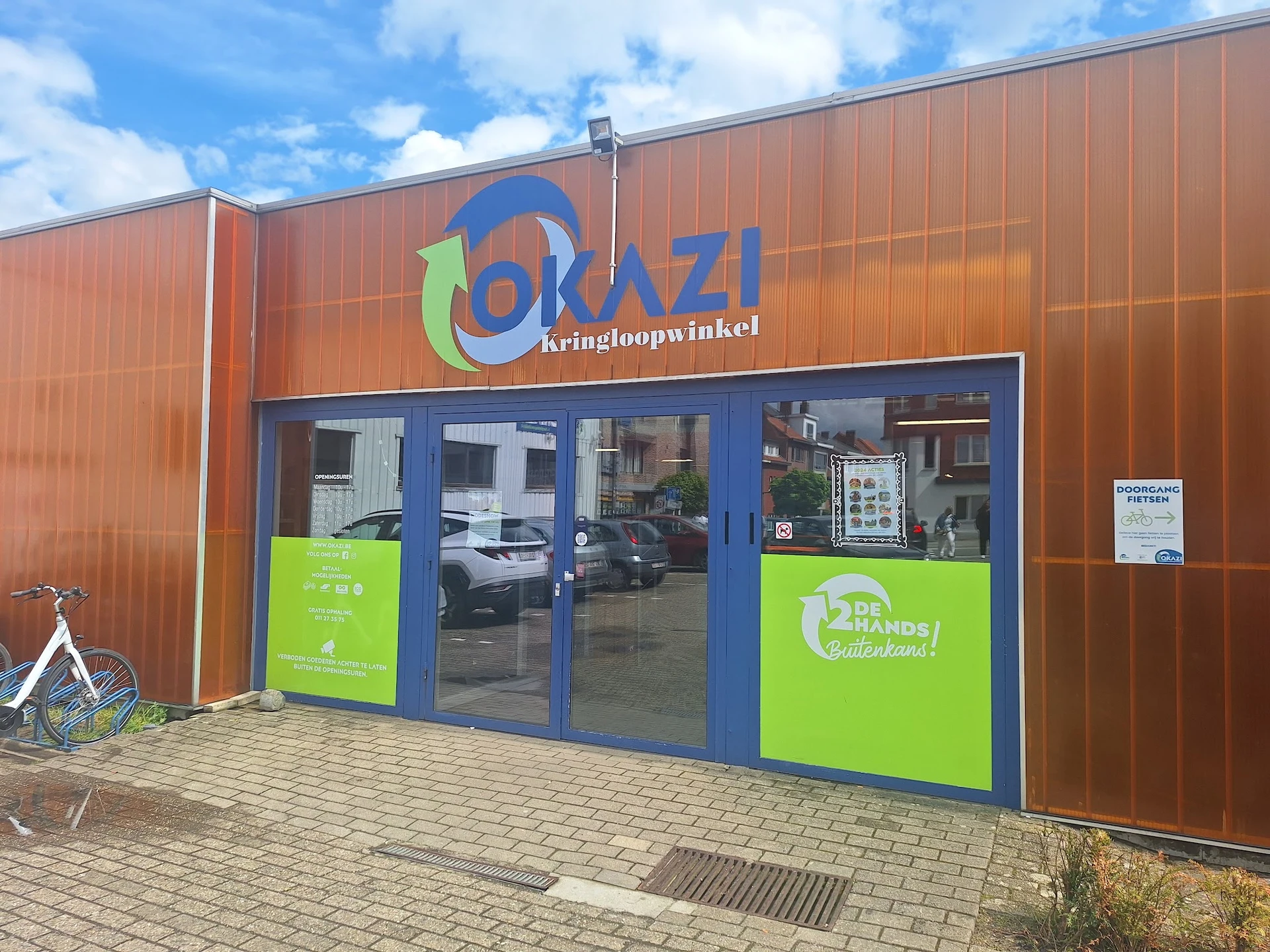 Voorgevel van kringloopwinkel met bruine golfmetalen wanden, blauwe deuren en groen accent met logo