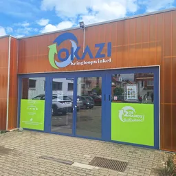 Voorgevel van kringloopwinkel met bruine golfmetalen wanden, blauwe deuren en groen accent met logo