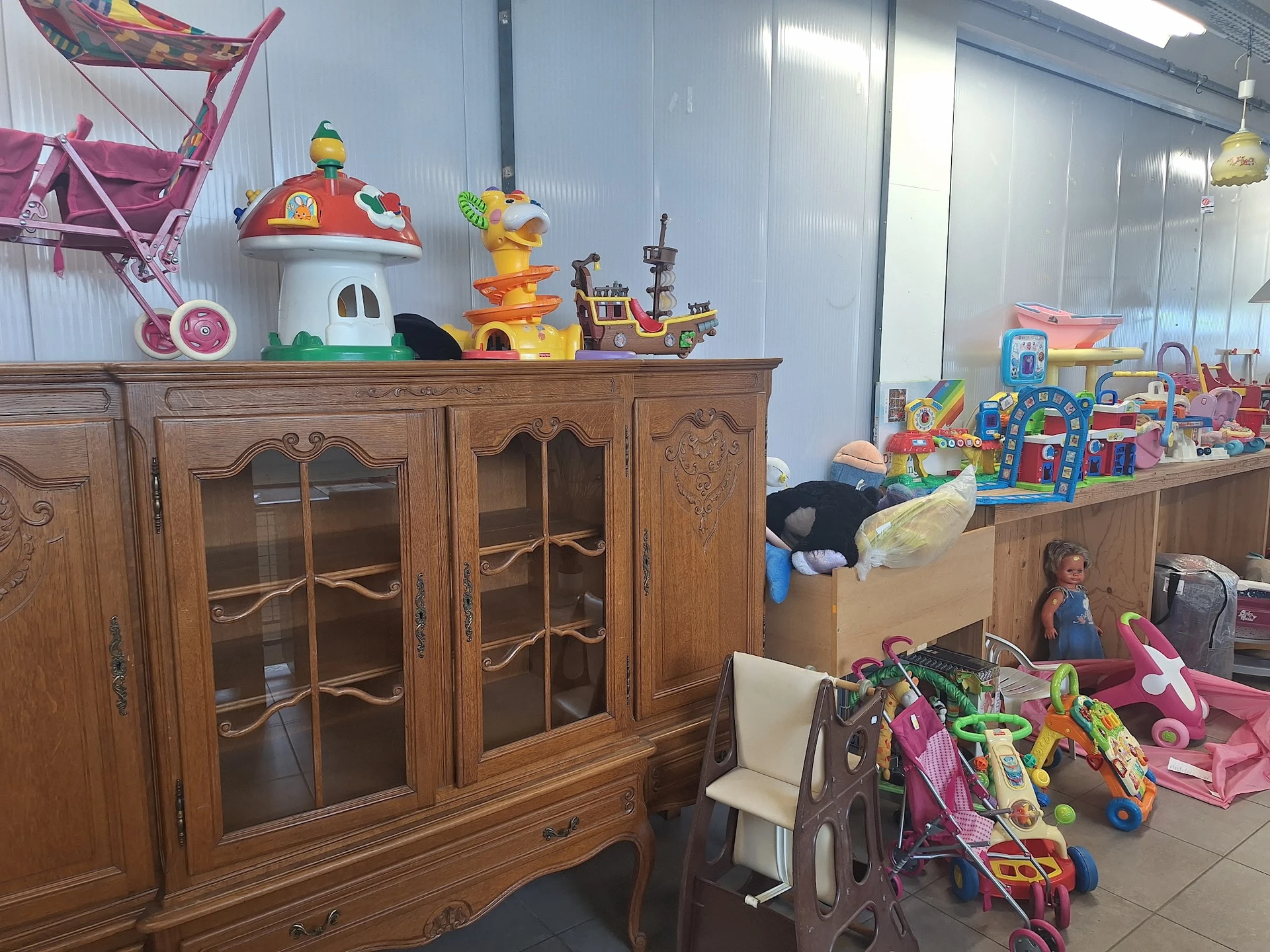 Speelgoed en kinderspullen uitgestald in een kringloopwinkel, met houten meubels, poppen, speelgoedhuizen en voertuigen