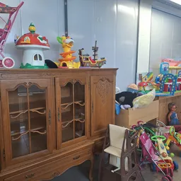Speelgoed en kinderspullen uitgestald in een kringloopwinkel, met houten meubels, poppen, speelgoedhuizen en voertuigen