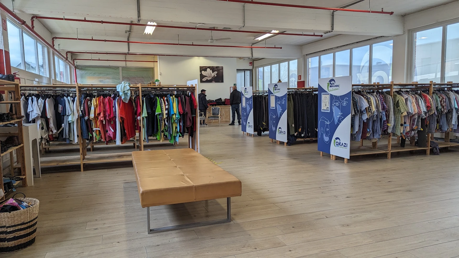 Ruime winkelruimte met kledingrekken aan beide zijden en houten bank in het midden