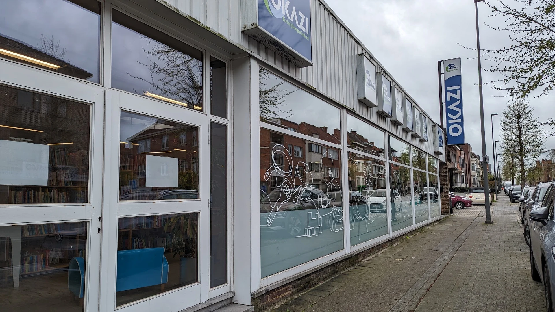 Winkelpui van kringloopwinkel met grote ramen, witte kozijnen en blauwe belettering, aan een winkelstraat