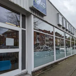 Winkelpui van kringloopwinkel met grote ramen, witte kozijnen en blauwe belettering, aan een winkelstraat