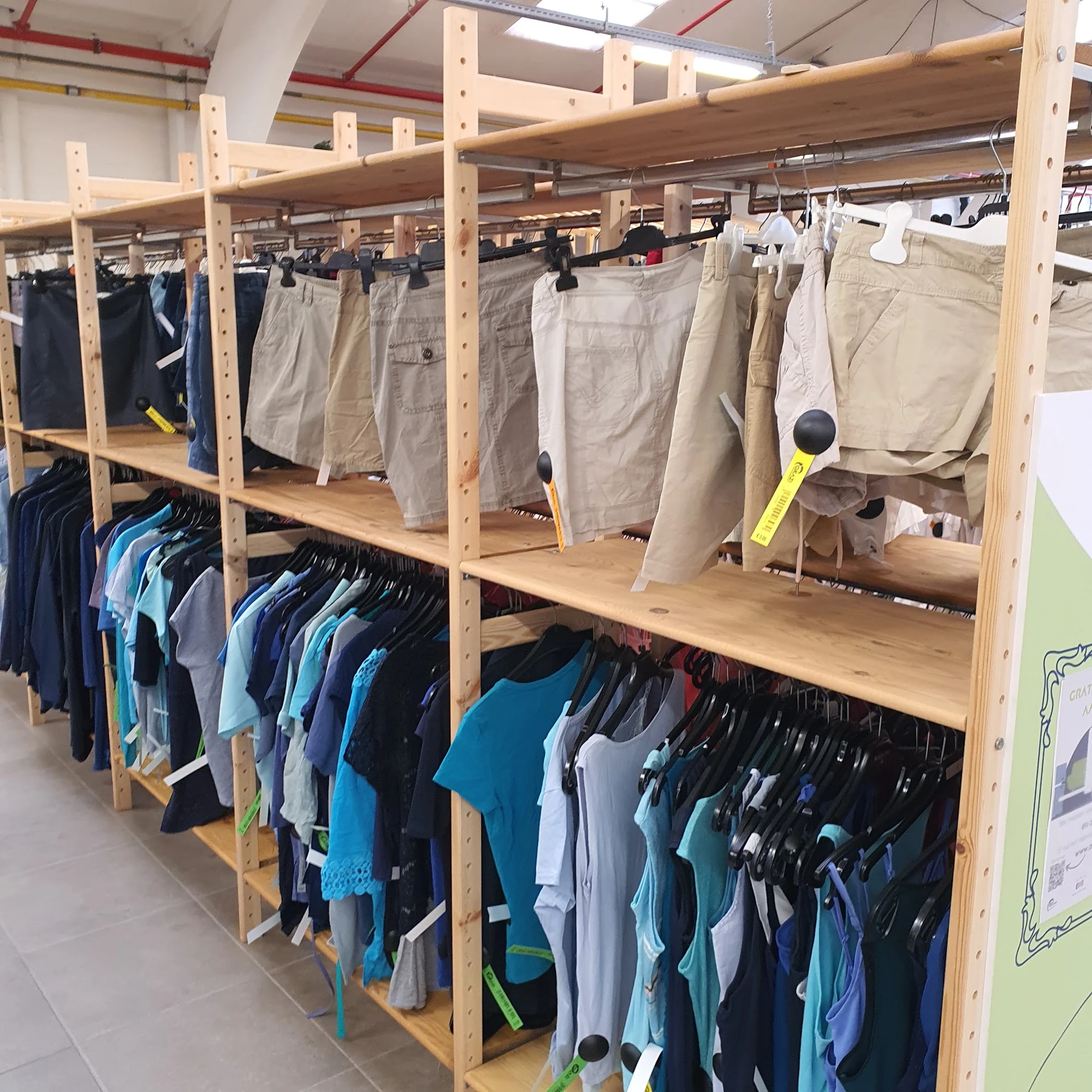 Houten stellingen met tweedehands kleding: broeken opgehangen aan de bovenkant, T-shirts en andere kledingstukken aan hangers