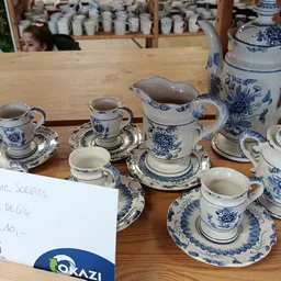 Uitgestalde serviesset met blauwe decoratie: kopjes, schotels, kannen en theepot op houten tafel