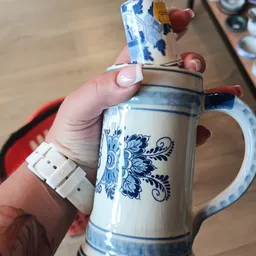 Close-up van een blauw-wit porseleinen kan met decoratief patroon, gehouden in een hand