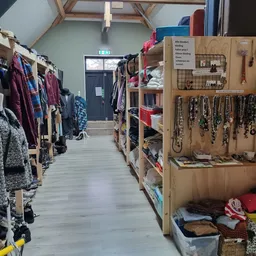 Winkelinterieur met kledingrekken links, houten wandpaneel met sieraden rechts, en tassen onderaan