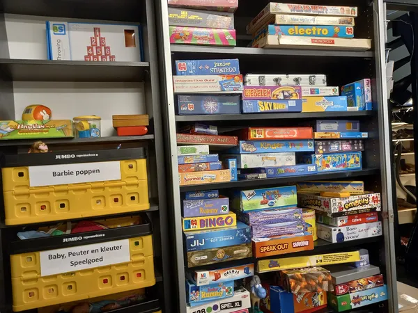 Stellingen met uitgestalde vintage spellen en bordspellen in dozen, waaronder Barbie poppen en kinderspeelgoed