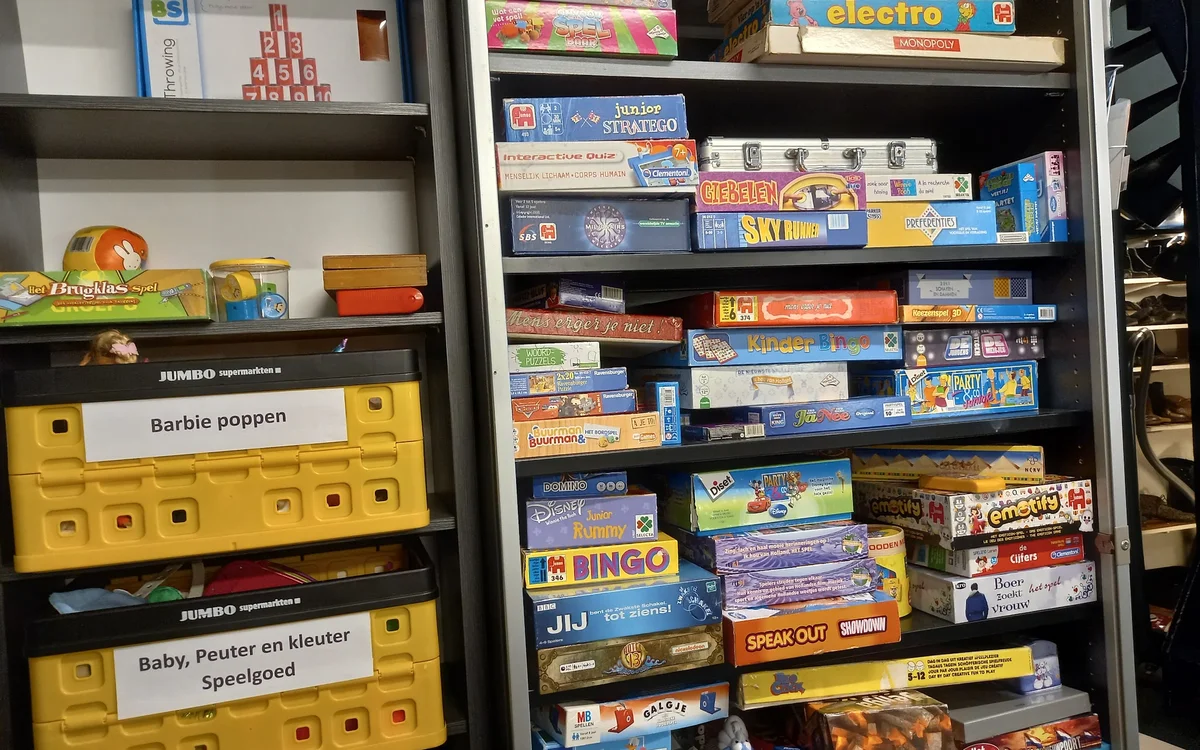 Stellingen met uitgestalde vintage spellen en bordspellen in dozen, waaronder Barbie poppen en kinderspeelgoed