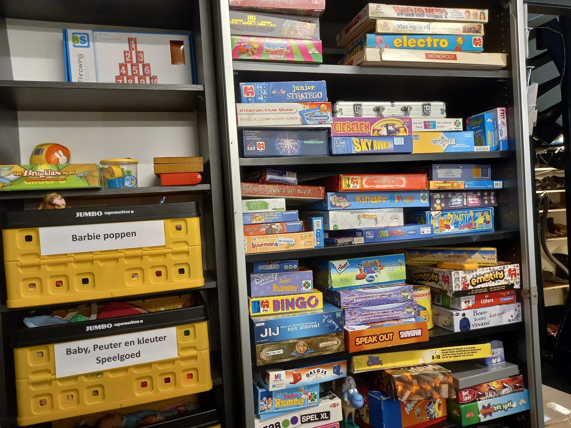 Stellingen met uitgestalde vintage spellen en bordspellen in dozen, waaronder Barbie poppen en kinderspeelgoed