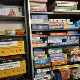 Stellingen met uitgestalde vintage spellen en bordspellen in dozen, waaronder Barbie poppen en kinderspeelgoed