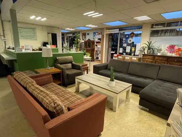 Zithoek in kringloopwinkel met bruine fauteuil, grijze bank, houten salontafel en cactus