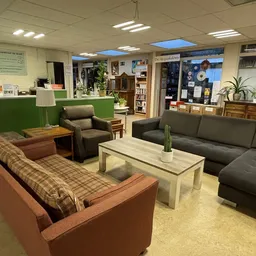 Zithoek in kringloopwinkel met bruine en grijze zitmeubels, salontafel en planten