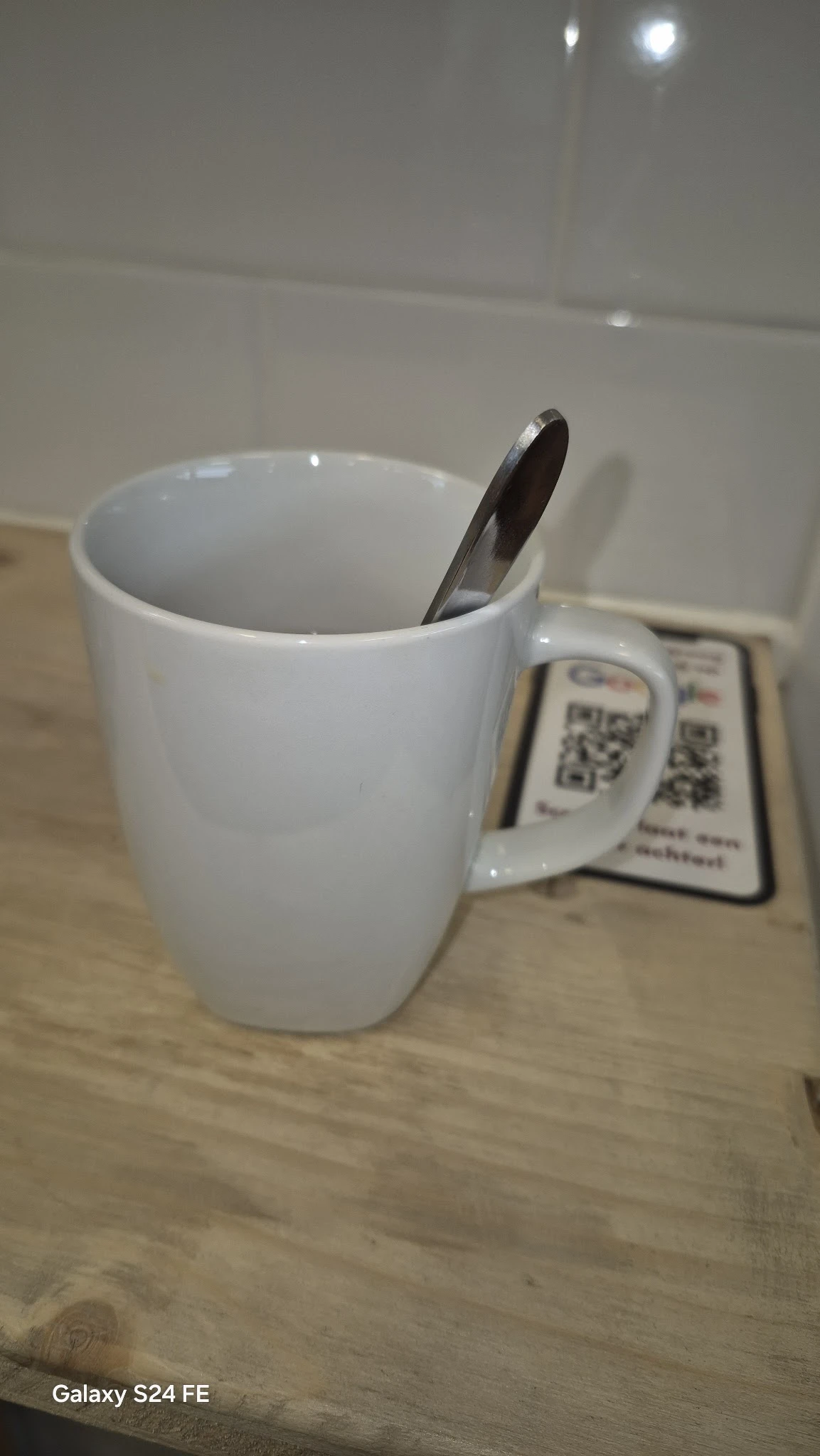 Witte keramische mok met zwarte lepel en QR-codes op een houten tafel