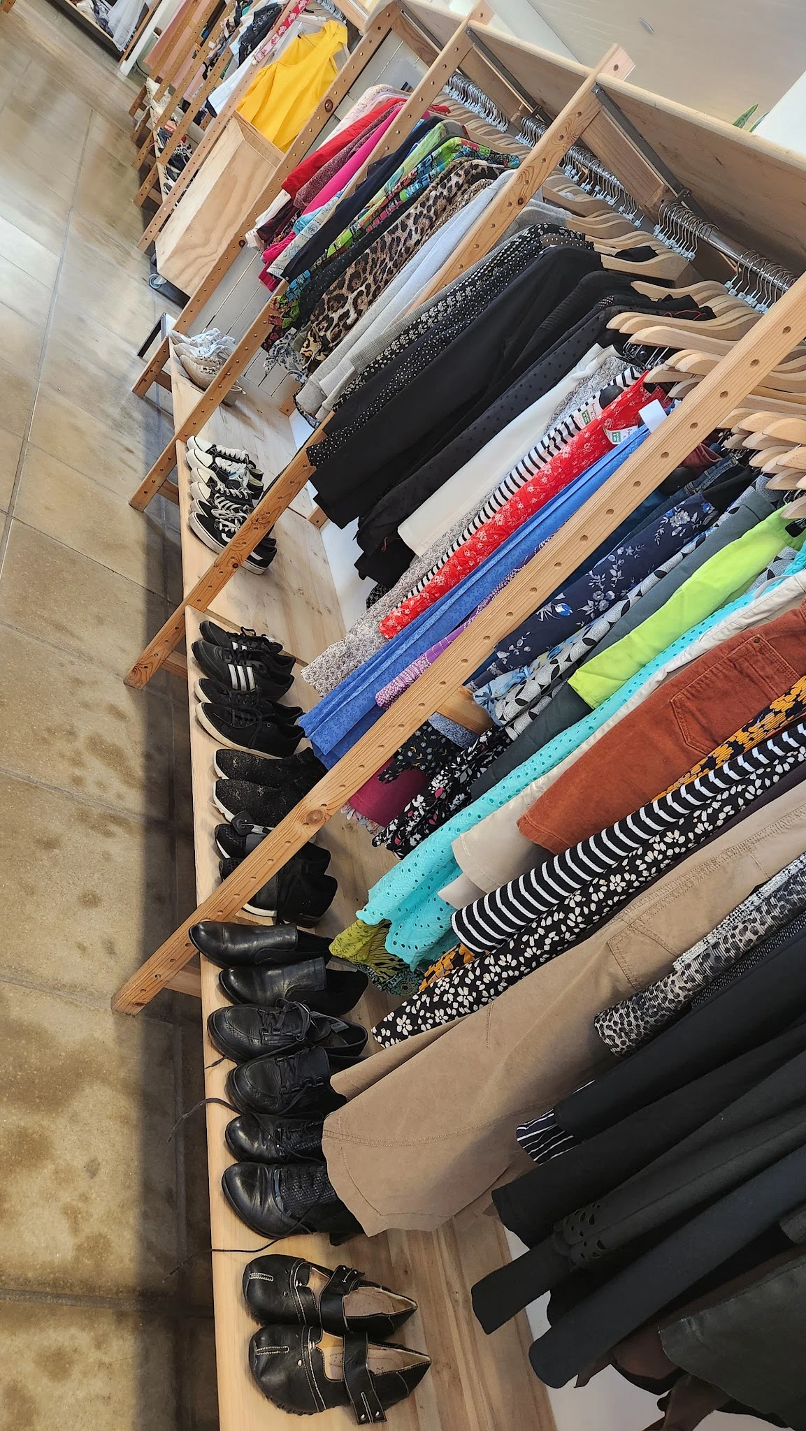 Uitgestalde kleding op houten rekken, waaronder schoenen, broeken en shirts in verschillende kleuren