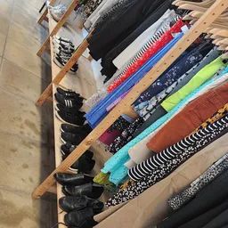Uitgestalde kleding op houten rekken, waaronder schoenen, broeken en shirts in verschillende kleuren