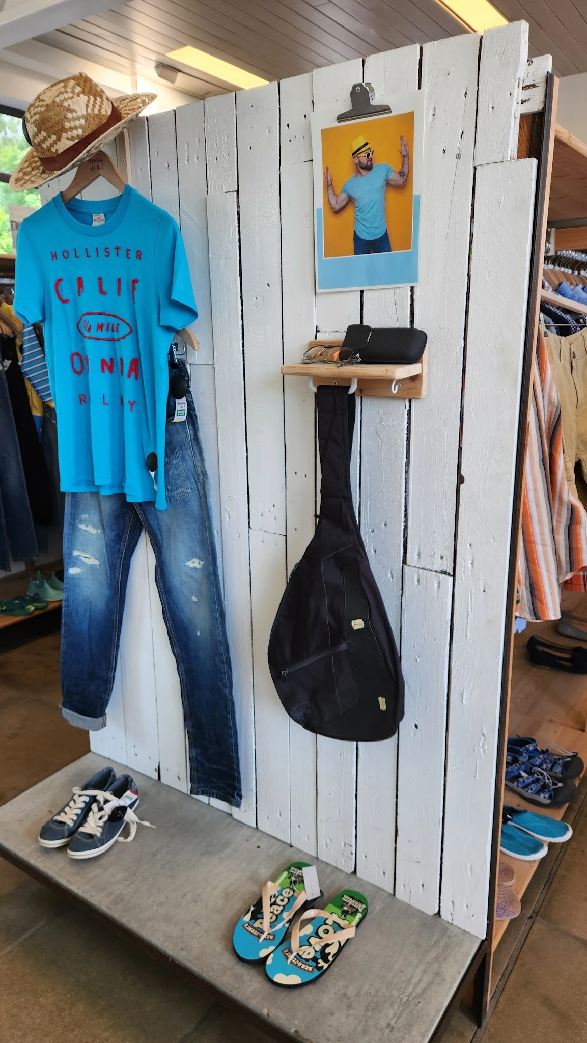 Tweedehands kleding en een gitaartas opgehangen aan een witte wand in de winkel