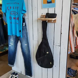 Tweedehands kleding en een gitaartas opgehangen aan een witte wand in de winkel