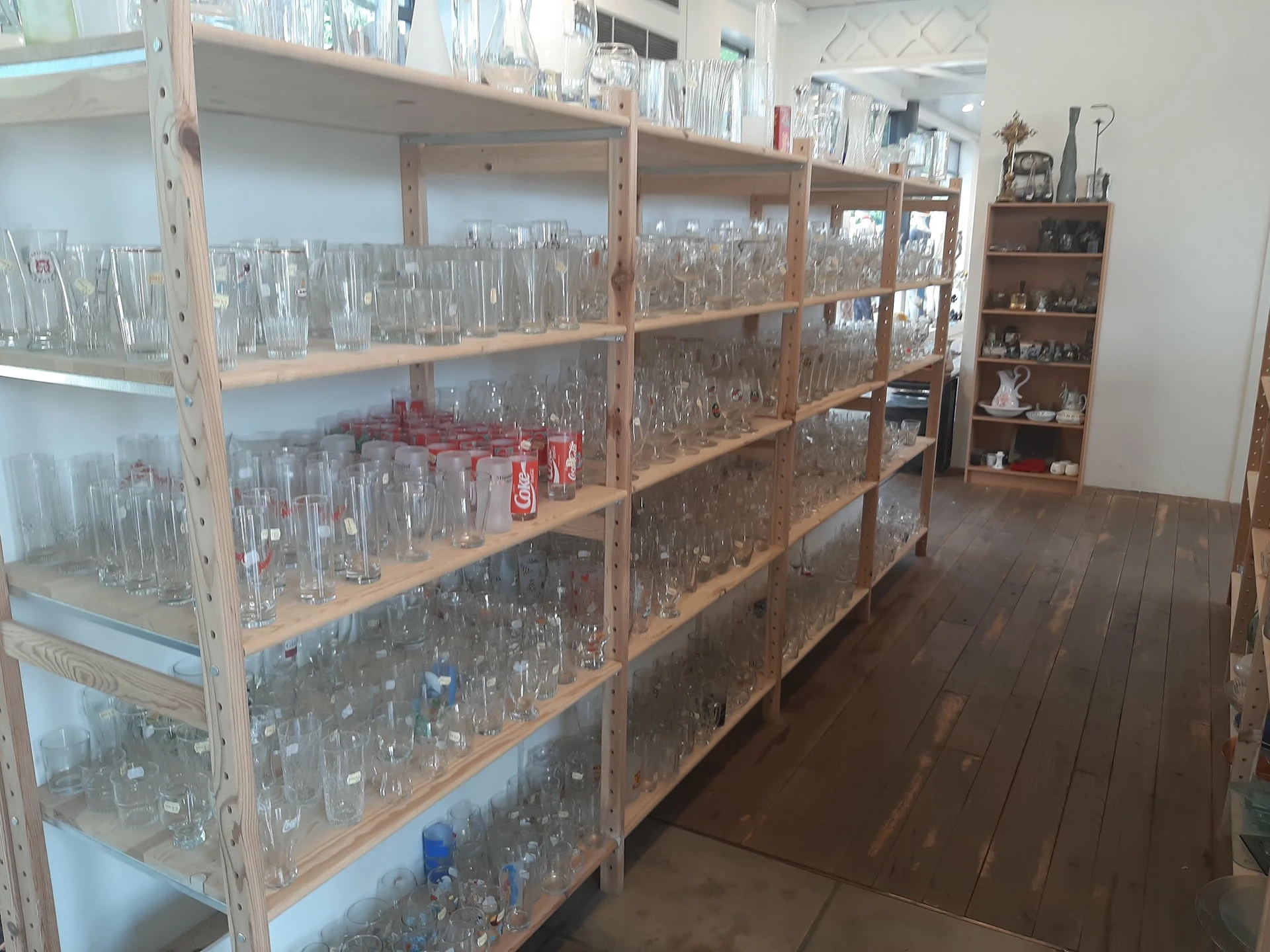 Houten stellingen met grote verzameling glazen flessen en bokalen, georganiseerd op meerdere niveaus