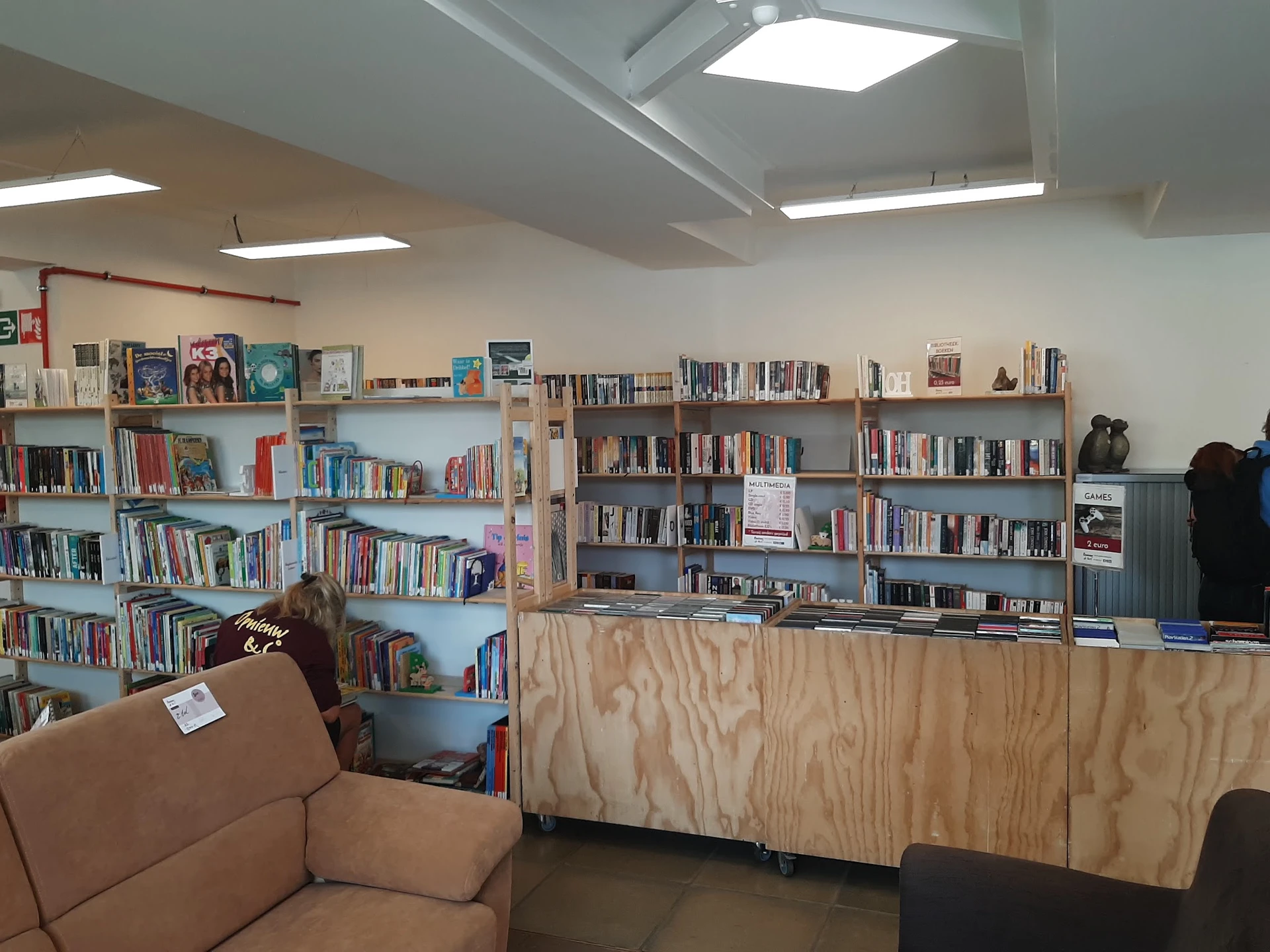 Boekenrekken en kasten vol met boeken en media in een bibliotheekachtige ruimte met zitbank