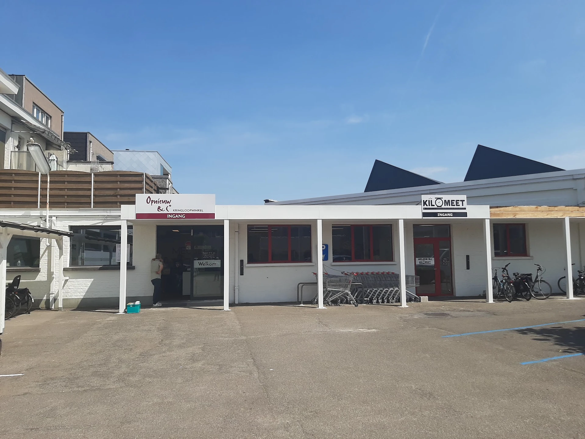 Witte gevel van kringloopwinkel met terrasoverkapping, fietsen en signage 'Opnieuw' en 'KILOMEET'