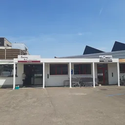 Witte gevel van kringloopwinkel met terrasoverkapping, fietsen en signage 'Opnieuw' en 'KILOMEET'