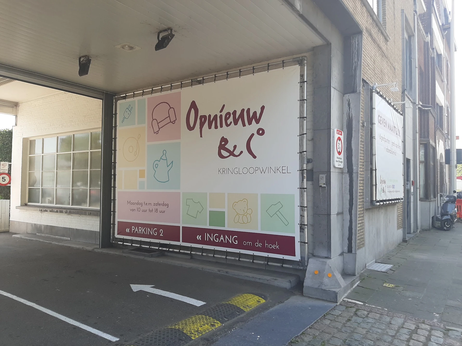 Winkelgevel van kringloopwinkel met grote uitstalraam en logo 'Opnieuw & Co' met gekleurde icoontjes