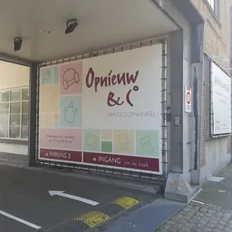 Winkelgevel van kringloopwinkel met grote uitstalraam en logo 'Opnieuw & Co' met gekleurde icoontjes
