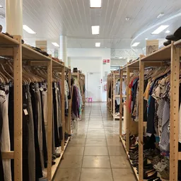 Lange gang met houten stellingen vol tweedehands kleding aan beide zijden, goed verlicht