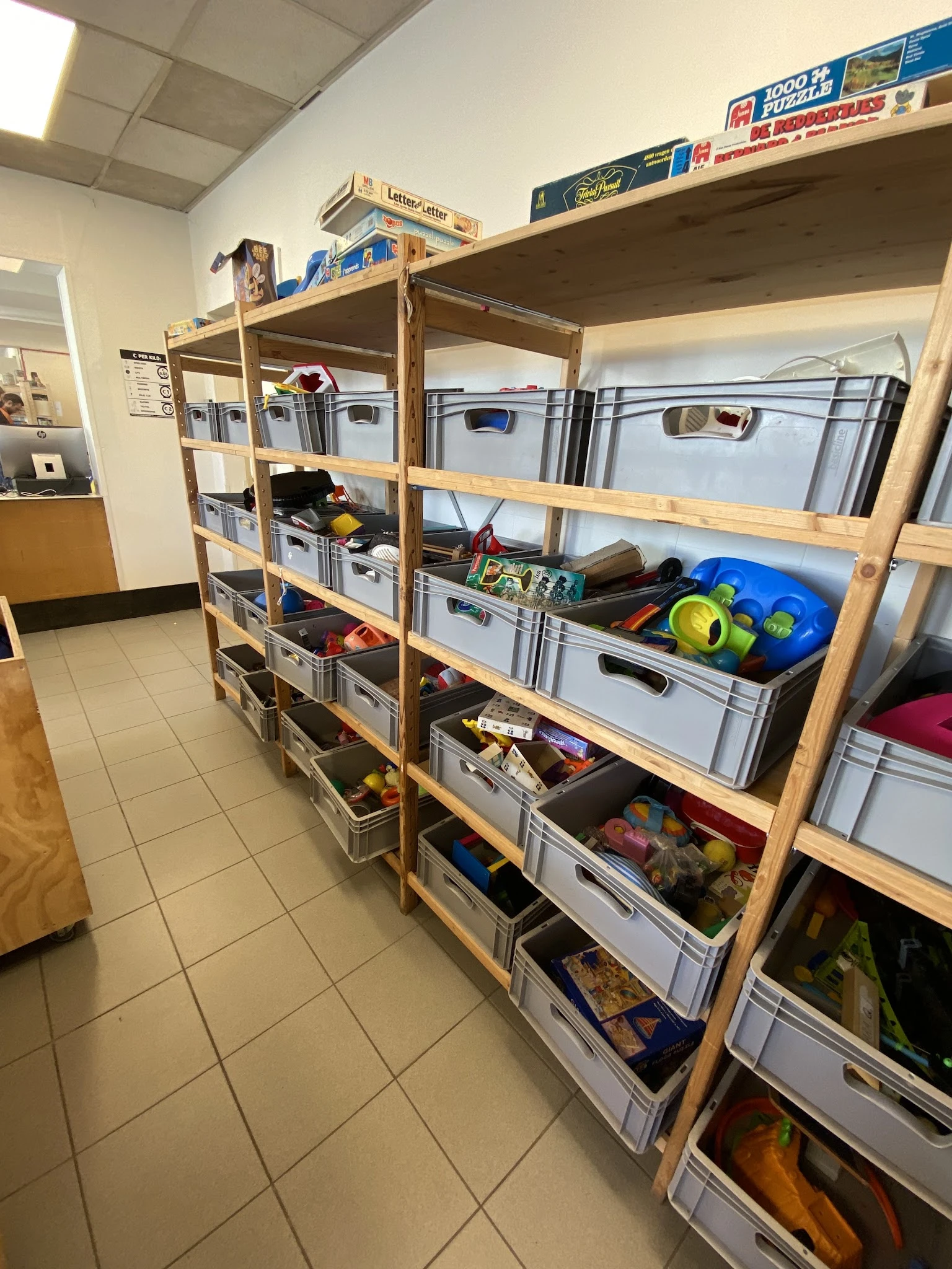 Houten stellingen met grijze plastic opbergbakken en diverse spullen in een kringloopwinkel