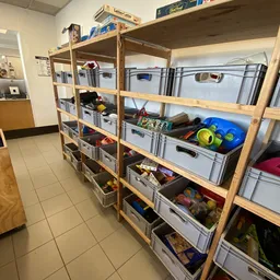 Houten stellingen met grijze plastic opbergbakken en diverse spullen in een kringloopwinkel