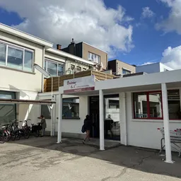 Winkelvoorgevel met witte afdakking, glazen deuren en ramen, fietsenstalling aan zijkant, parkeerplaatsen en winkelwagentjes