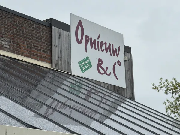Uithangbord van Opnieuw & Co op een dakrand met bakstenen gevel ernaast