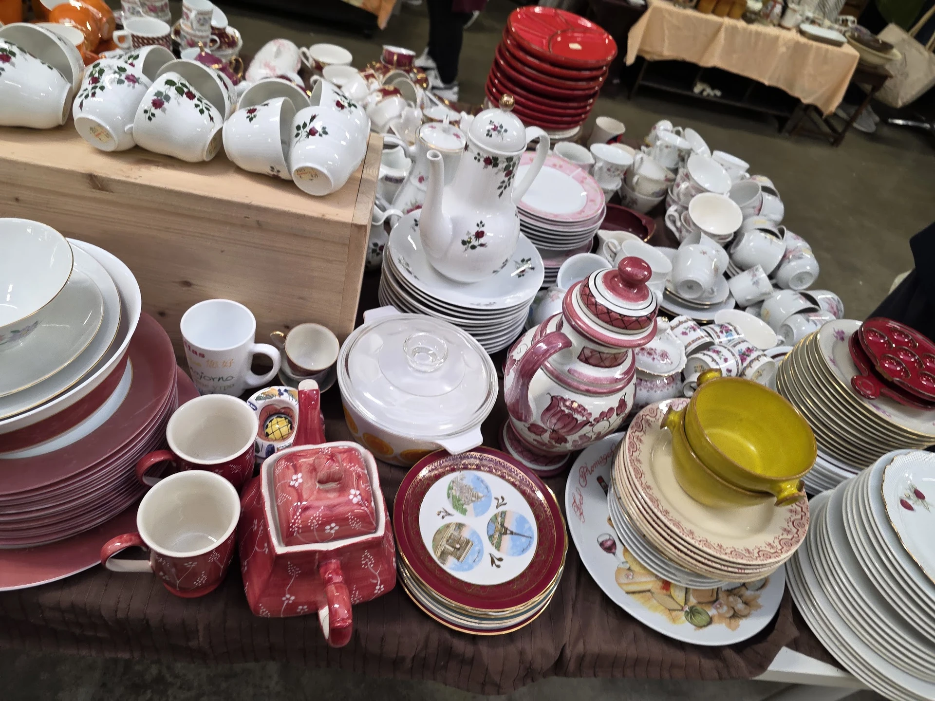 Uitgestalde serviesgoed en keukengerei op een tafel: borden, kopjes, schalen en ketels in wit, rood en roze