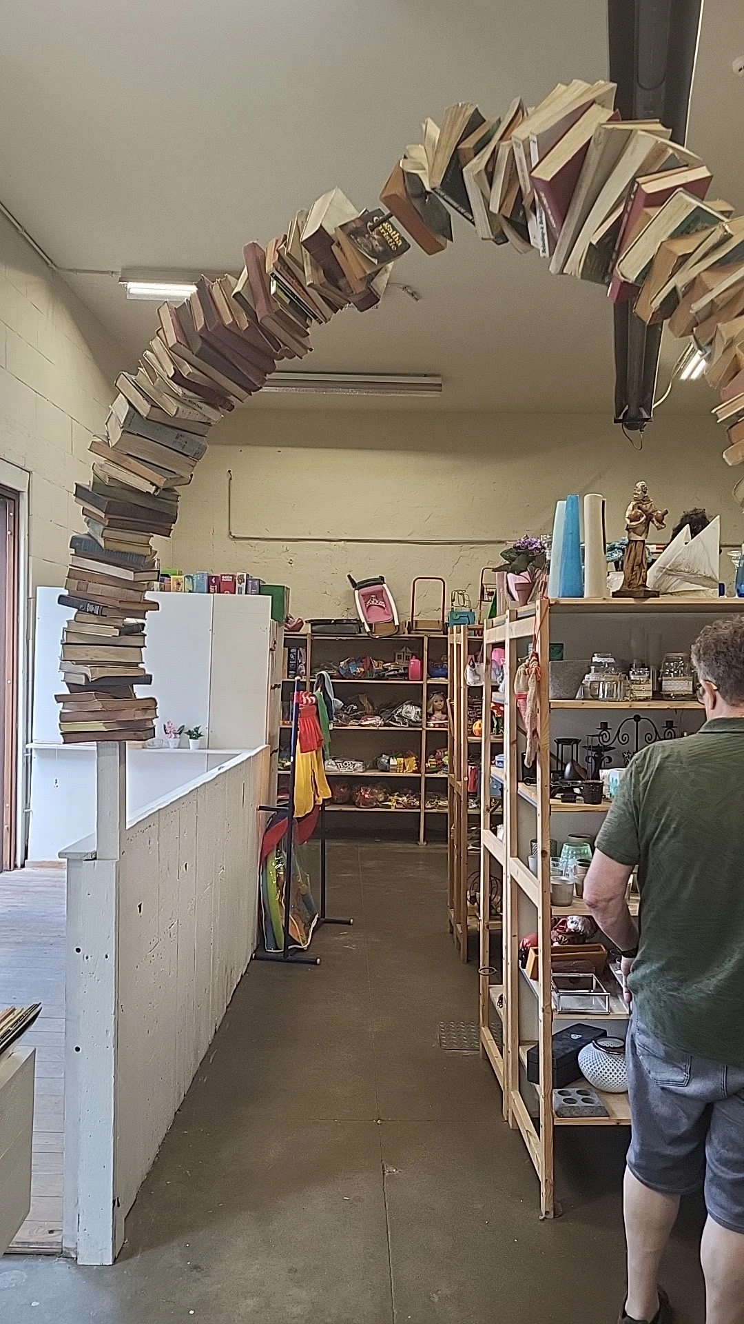 Winkelvloer met stellingen vol spullen, boeken gestapeld tegen muur, diverse artikelen en decoraties zichtbaar