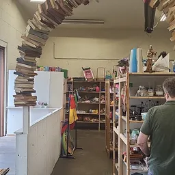 Winkelvloer met stellingen vol spullen, boeken gestapeld tegen muur, diverse artikelen en decoraties zichtbaar
