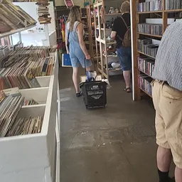 Winkelinterieur met cd- en dvd-rekken, klanten tussen stellingen met winkelwagen