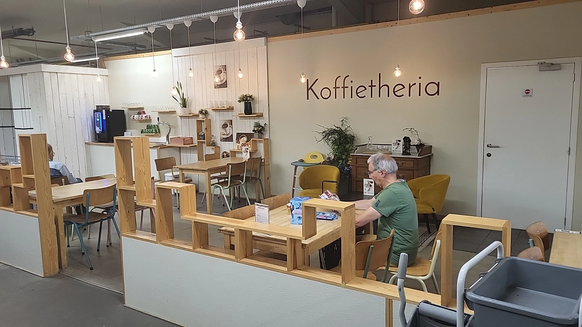 Koffietharia-hoek met houten tafels, gele stoelen en een klant aan het werk