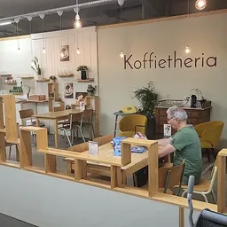 Koffietharia-hoek met houten tafels, gele stoelen en een klant aan het werk