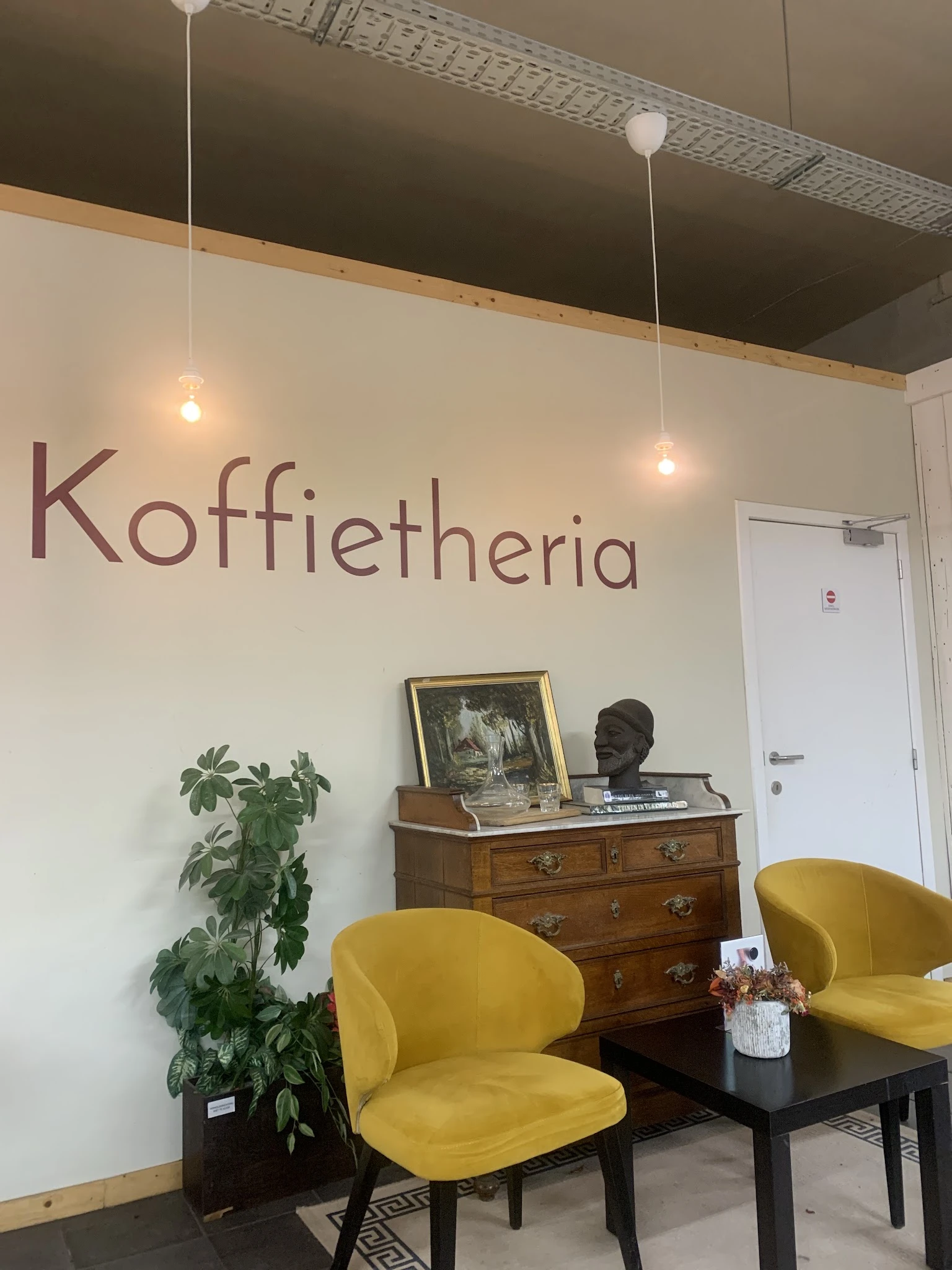 Interieur van koffieplek met gele stoelen, houten kast en wanddecoratie met het woord 'Koffietheria'