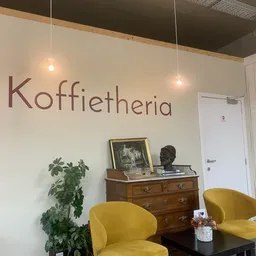 Interieur van koffieplek met gele stoelen, houten kast en wanddecoratie met het woord 'Koffietheria'