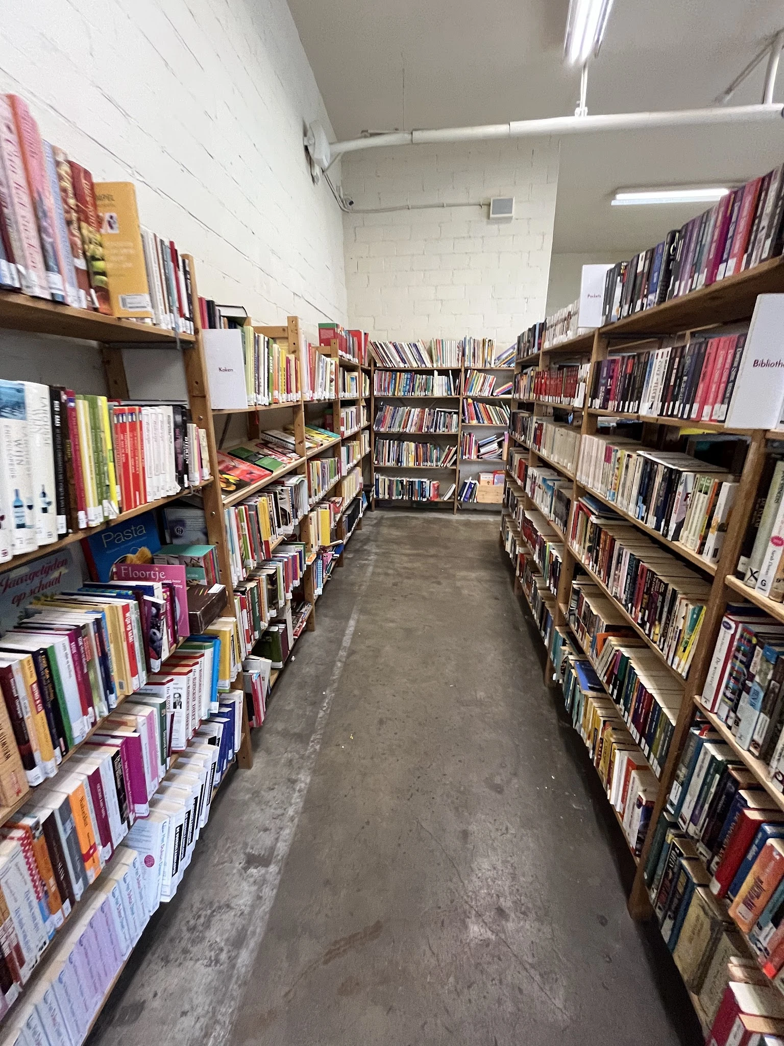 Gangpad tussen houten stellingen vol boeken in kringloopwinkel
