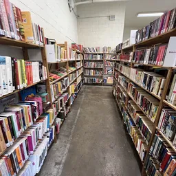 Gangpad tussen houten stellingen vol boeken in kringloopwinkel