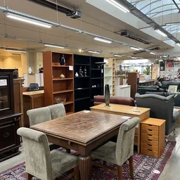 Winkelvloer met houten eettafel, stoelen en kasten met huisraad in een kringloopwinkel