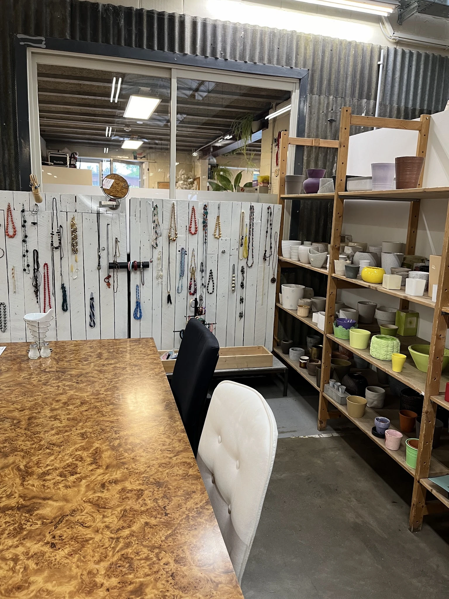 Winkelinterieur met sieradendisplay aan witte muur links, houten stellingen met servies en huishoudartikelen rechts, kurken v