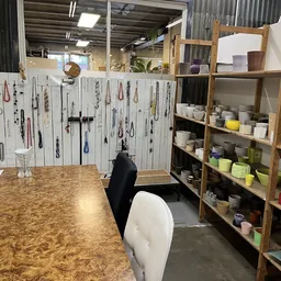 Winkelinterieur met sieradendisplay aan witte muur links, houten stellingen met servies en huishoudartikelen rechts, kurken v