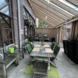 Overdekt terras met tafels en stoelen, uitzicht op winkelruimte met stellingen en winkelartikelen