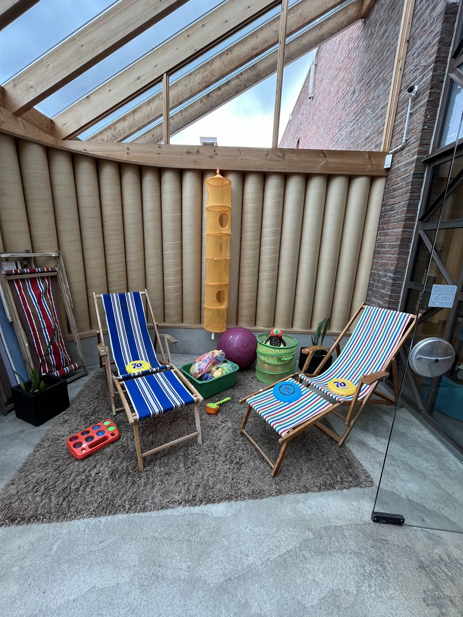 Tweedehands tuinmeubelen: ligbedden met blauw-witte strepen, paarse bal, groene emmer en ander tuingereedschap op betonvloer